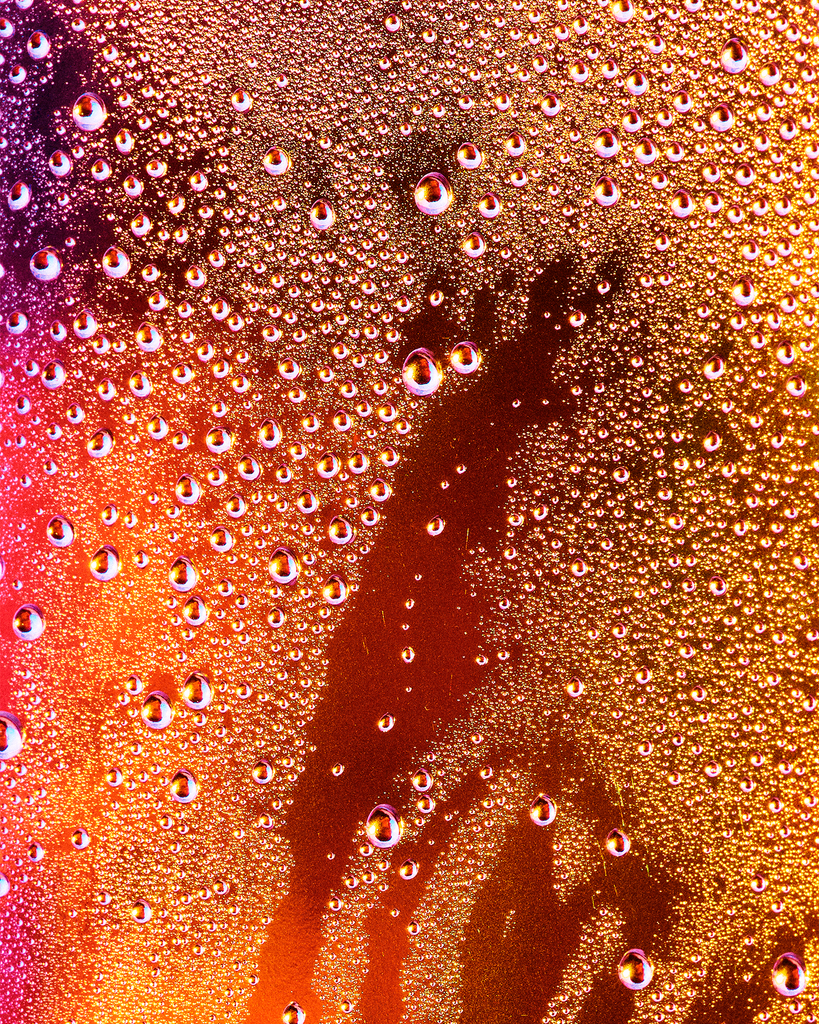 Joel Dixon, a graduate artist in the UK captures a close-up of condensation droplets on a glass surface, where vibrant orange and yellow lighting create an abstract pattern. This mesmerizing piece is part of the graduate artworks for sale by The Graduate Gallery.
