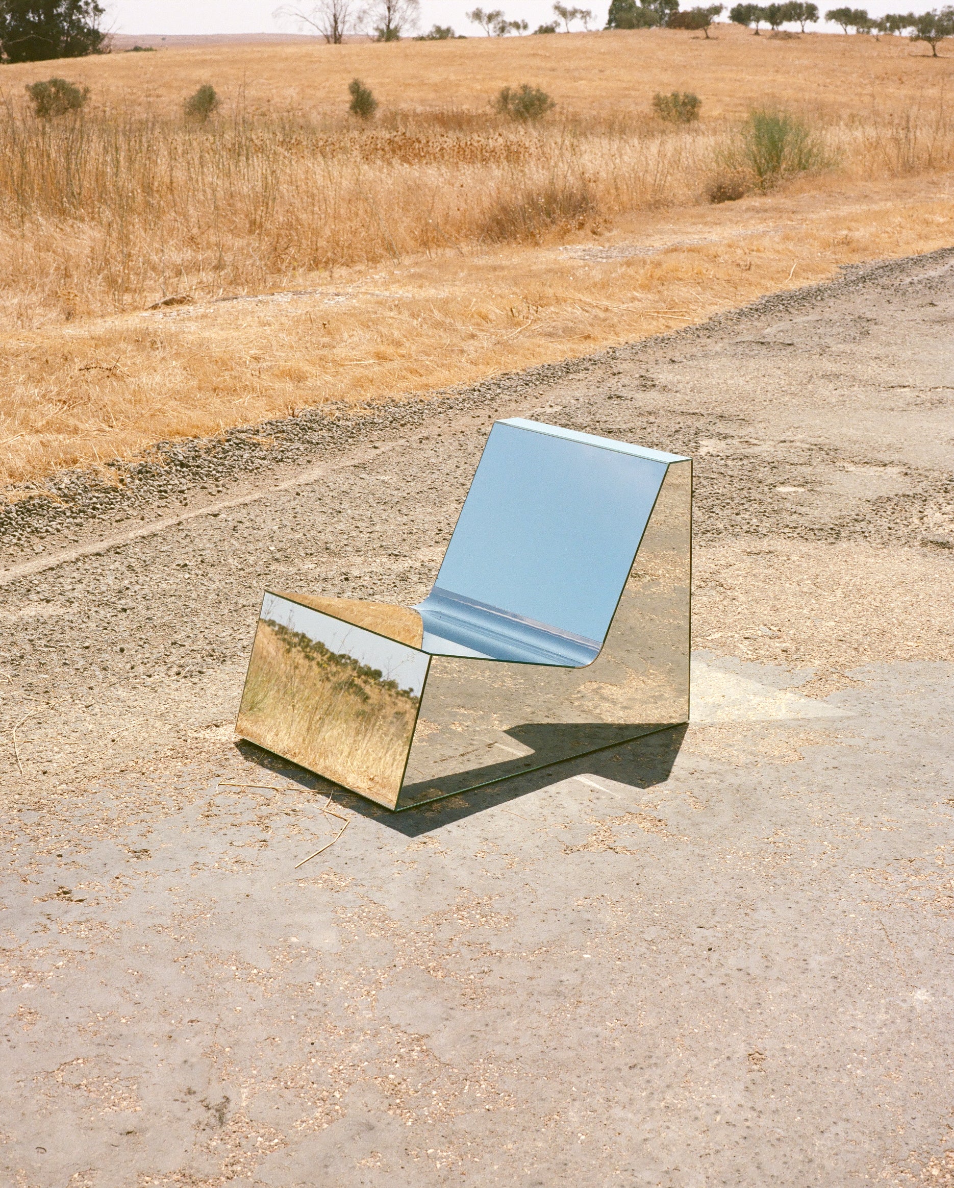 Discover a modern chair with a minimalist design, featuring a reflective mirror surface. Its angular shape creates a geometric aesthetic, set against a plain white background. This stunning piece of furniture is available for sale by The Graduate Gallery.