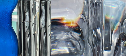 Created by a talented graduate artist in the UK, this close-up features abstract glass and plastic objects with distorted reflections. A blue textured surface graces the left, while wavy glass and light playfully distort vibrant colors on the right, available through The Graduate Gallery.