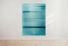 An abstract artwork by a graduate artist in the UK features horizontal bands of blue. The colors blend and blur, creating a dynamic, textured effect. Displayed with small metal clips at the corners, this piece is part of the graduate artworks for sale by The Graduate Gallery.