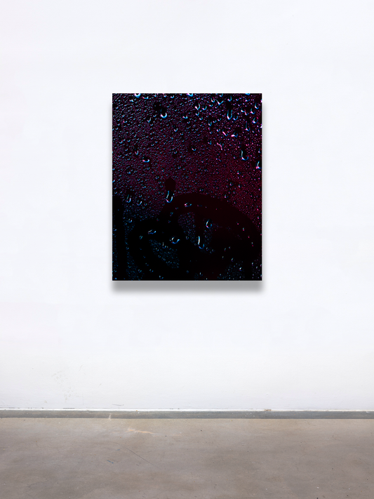 A graduate artwork by Joel Dixon, presented with The Graduate Gallery. The piece features a dark, textured surface adorned with glistening water droplets, set against deep hues of black, purple, and red. The abstract composition evokes a moody, atmospheric tone, with the droplets adding a sense of depth and tactile contrast. Displayed on a minimal white gallery wall, the work draws attention to its intricate details and reflective surface.