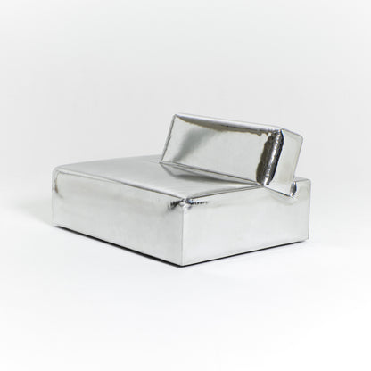 A modern, metallic couch from Project 213A a European design house launched in 2021, boasts a shiny silver finish and angular design. With its rectangular backrest, this piece of furniture stands elegantly against a plain white background.