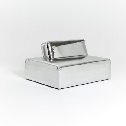 A modern, metallic couch from Project 213A a European design house launched in 2021, boasts a shiny silver finish and angular design. With its rectangular backrest, this piece of furniture stands elegantly against a plain white background.