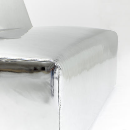 A modern, metallic couch from Project 213A a European design house launched in 2021, boasts a shiny silver finish and angular design. With its rectangular backrest, this piece of furniture stands elegantly against a plain white background.