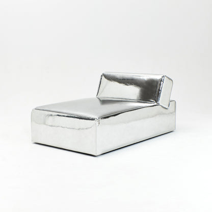 A modern, metallic couch from Project 213A a European design house launched in 2021, boasts a shiny silver finish and angular design. With its rectangular backrest, this piece of furniture stands elegantly against a plain white background.