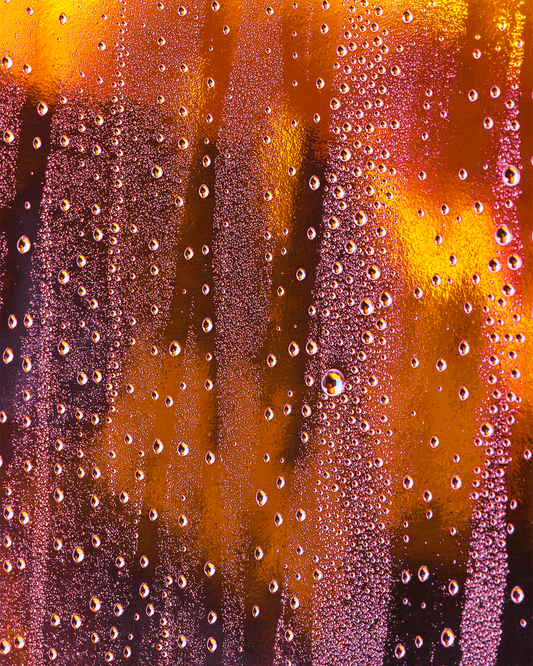 A graduate artist in the UK captures a close-up of condensation droplets on a glass surface, where vibrant orange and yellow lighting create an abstract pattern. This mesmerizing piece is part of the graduate artworks for sale by The Graduate Gallery.